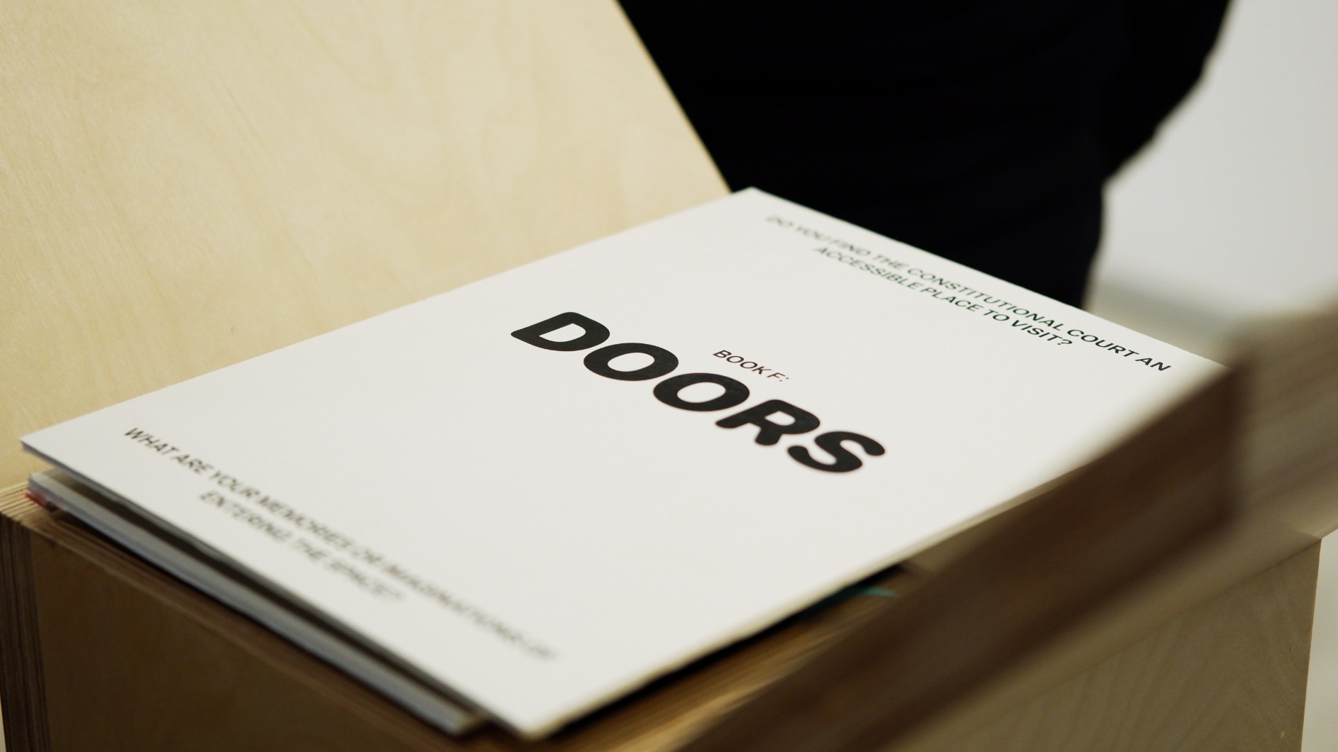 Photo of artwork fragment. Artwork is a series of 6 timber podiums. One podium interior is seen in this photo with book cover reading 'DOORS'.