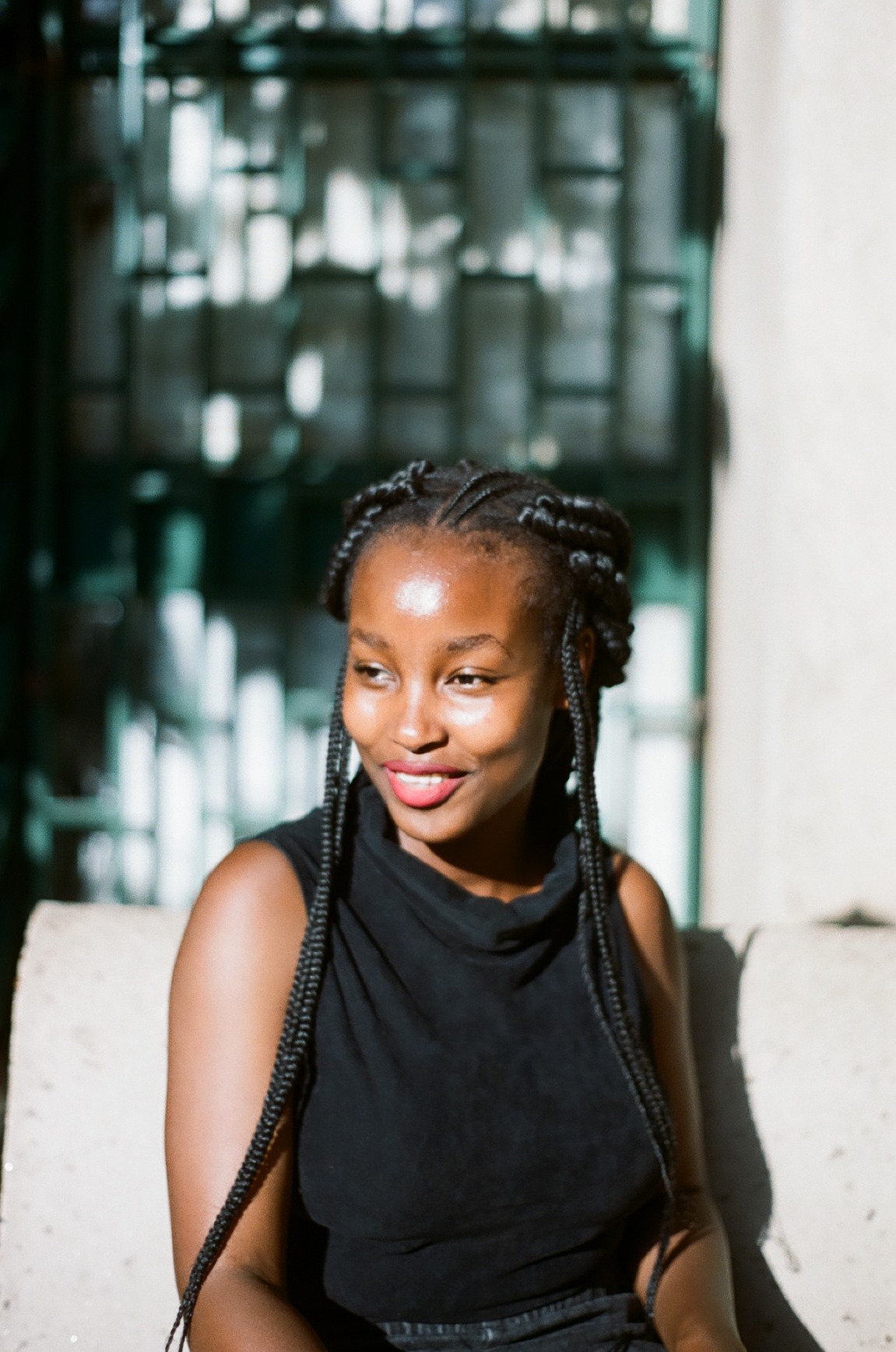 Photo portrait of young African woman smiling into distance with braids and a black top.