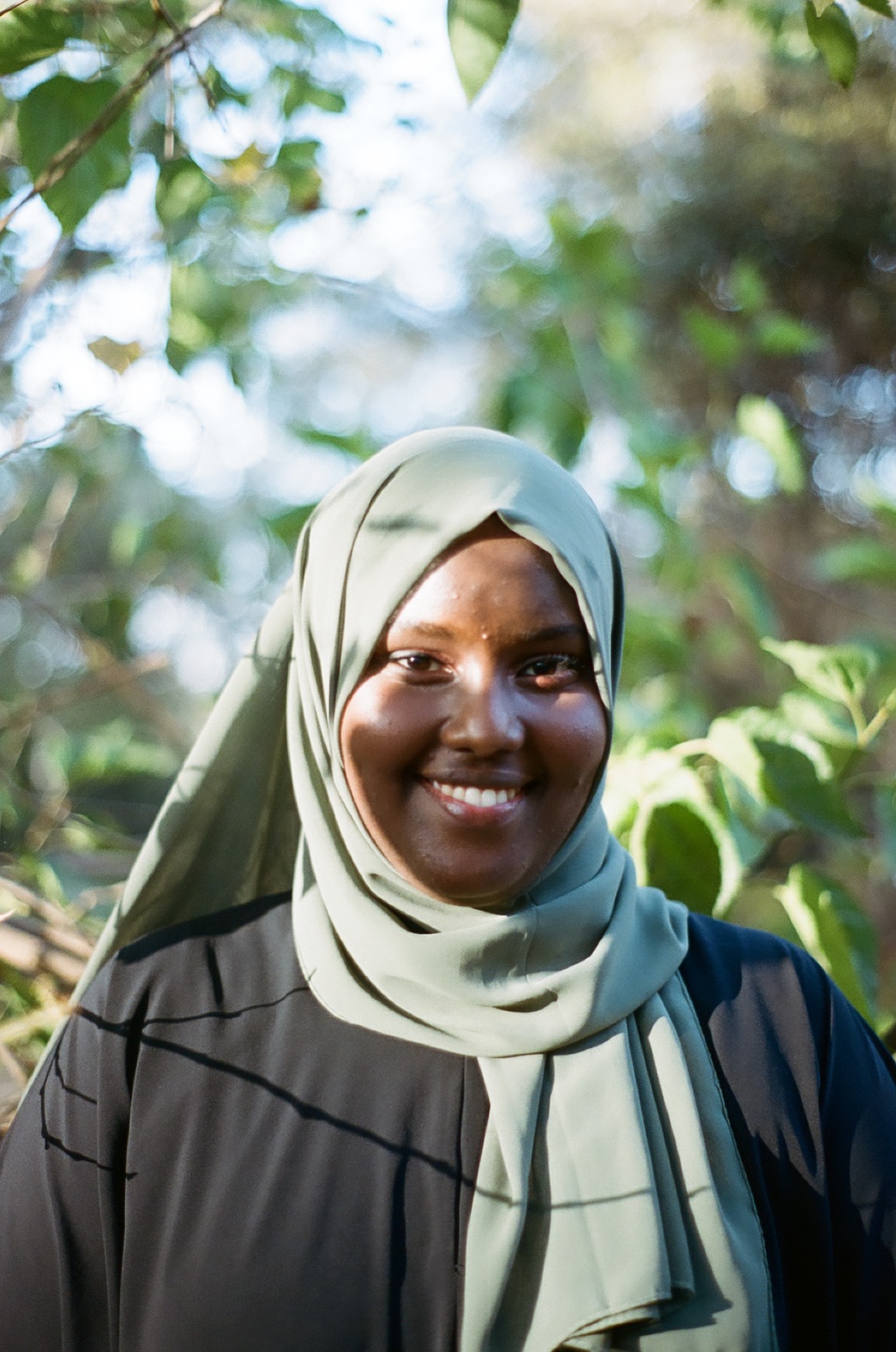 Photo portrait of young African woman smiling with an olive green head scard and black blouse.