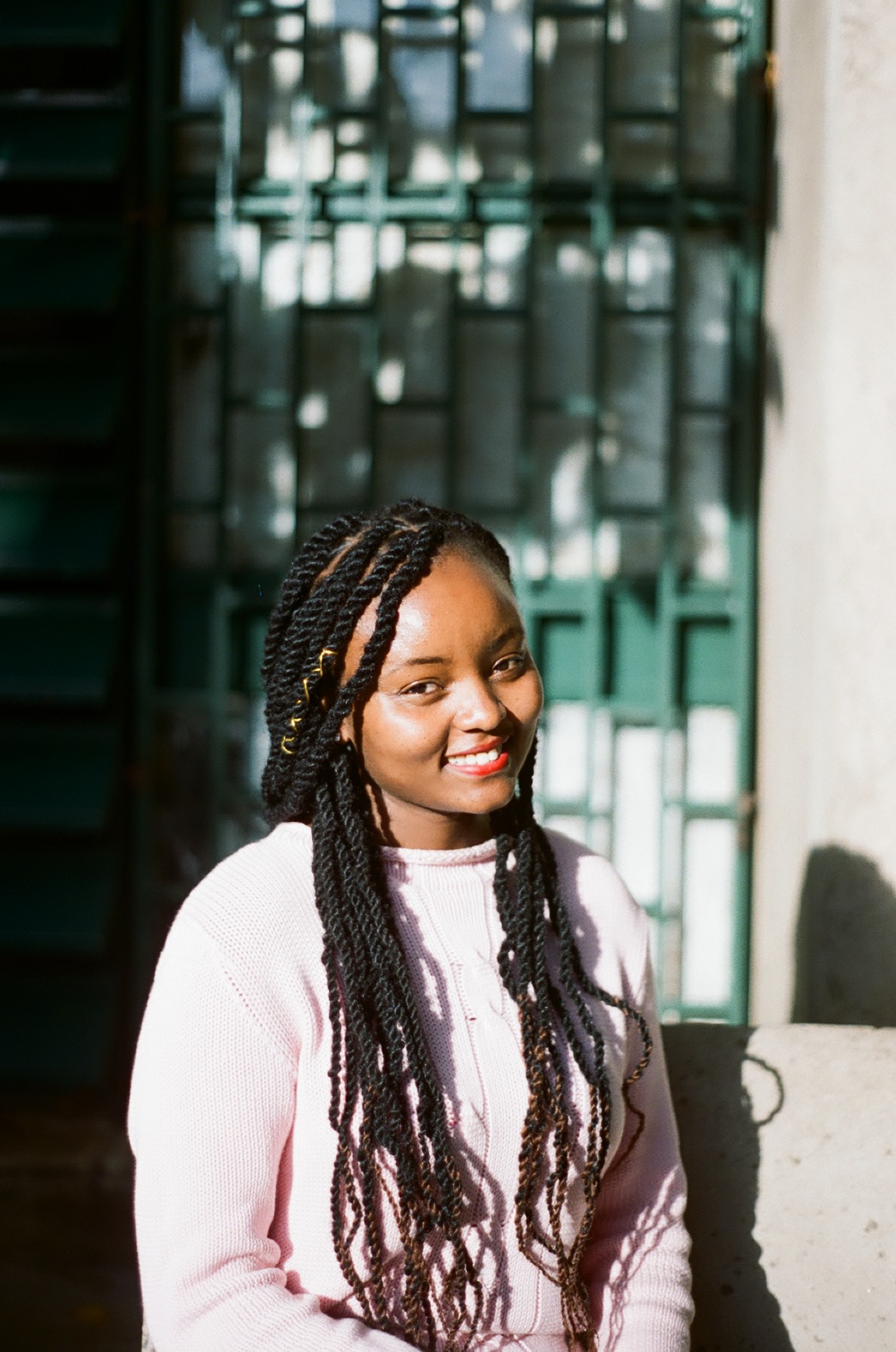 Photo portrait of young African woman smiling with braids and a pink jumper.