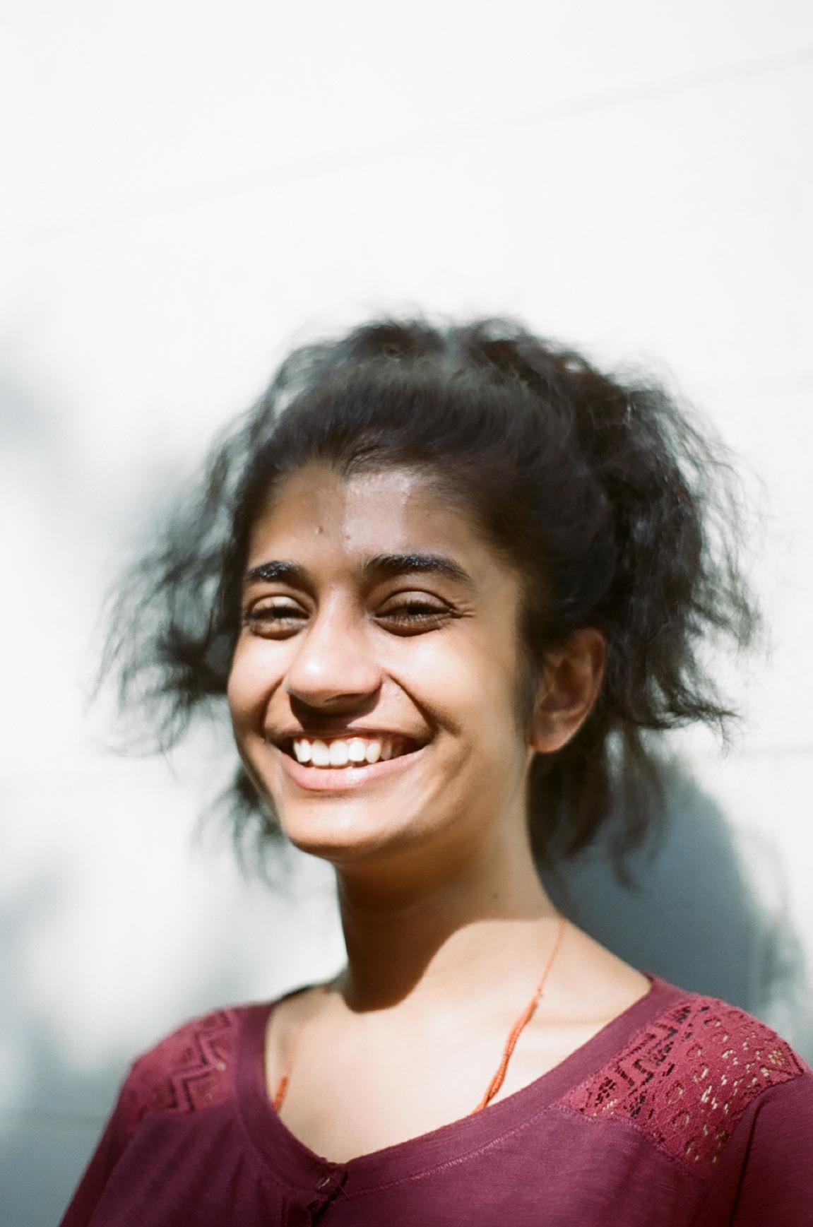 Photo portrait of young woman who is a person of colour, smiling with a maroon blouse.