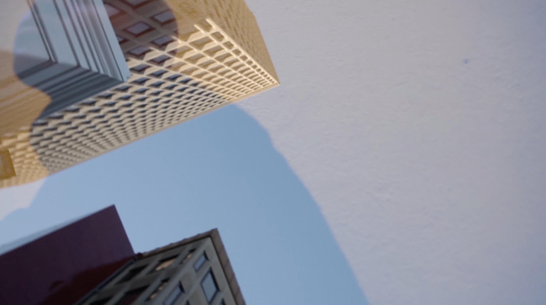 Still image from Ode to an Architect film showing the main protagonist silhouette overlayed on two buildings seen from the below on the street. The colours are pale blues, yellows and maroon.